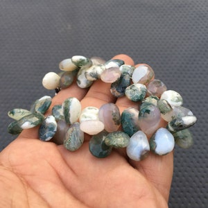 May include: A strand of moss agate beads in shades of green, white, and gray. The beads are irregularly shaped and have a natural, polished finish.