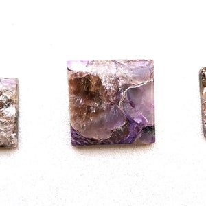 May include: Three square and rectangular shaped purple and brown gemstone cabochons. The stones have a swirling, layered pattern.