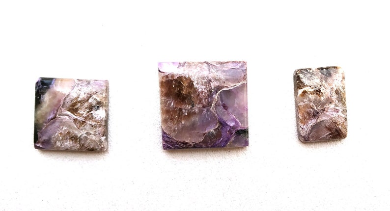 May include: Three square and rectangular shaped purple and brown gemstone cabochons. The stones have a swirling, layered pattern.