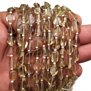 May include: A strand of light brown, faceted, teardrop-shaped gemstone beads. The beads are strung on a white thread.