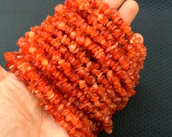 May include: A strand of orange carnelian chip beads. The beads are small and irregular in shape, and they are strung together on a clear thread.