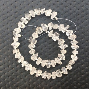 May include: A strand of clear quartz crystal beads, each bead is faceted and has a rough, irregular shape. The beads are strung on a thin wire and are arranged in a circular pattern.