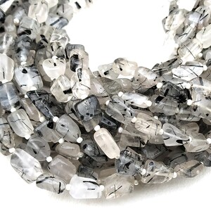 May include: A strand of faceted, clear quartz beads with black tourmaline inclusions. The beads are irregular in shape and have a natural, raw look.