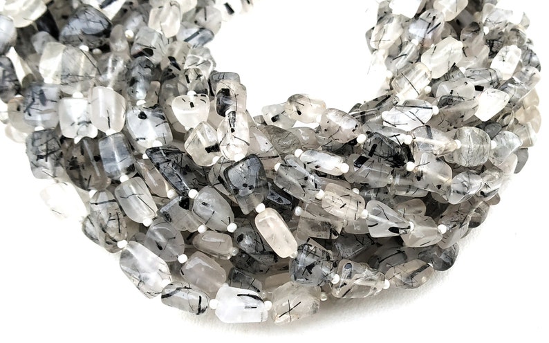 May include: A strand of faceted, clear quartz beads with black tourmaline inclusions. The beads are irregular in shape and have a natural, raw look.