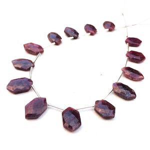 Puede incluir: Una hebra de cuentas de rubí facetadas, cada cuenta es de un color rojo púrpura intenso con un ligero brillo iridiscente. Las cuentas están enhebradas en un alambre de plata.