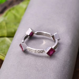 Peut inclure: Une bague en argent avec quatre pierres précieuses roses carrées serties dans la bande. La bande est décorée d'un motif floral délicat.