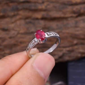 May include: A silver ring with a red oval gemstone set in a geometric design.