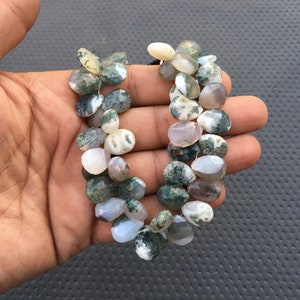 May include: A strand of moss agate beads, featuring a mix of green, white, and gray colors. The beads are irregularly shaped and have a natural, polished finish.