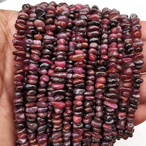 Può includere: Un filo di piccole perle di pietre preziose irregolari, rosse e viola. Le perle sono di circa 5 mm di dimensione e hanno una finitura liscia e lucida.