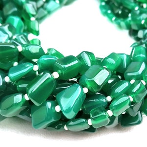 May include: A strand of green agate gemstone beads, each bead is a unique, irregular shape. The beads are polished and have a smooth, glossy finish.