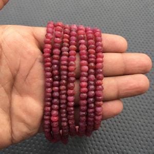 Puede incluir: Una hebra de cuentas de rubí rojo, facetadas y redondas, enhebradas en un hilo. Las cuentas tienen aproximadamente 4 mm de diámetro y se muestran en una mano.