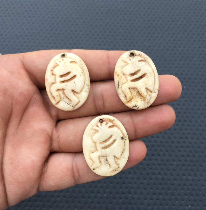 May include: Three oval-shaped pendants made of white bone with a carved design of a stylized animal figure. The pendants have a hole at the top for hanging.
