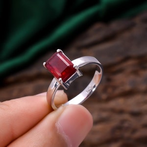 Może przedstawiać: Srebrny pierścionek z dużym, prostokątnym, czerwonym kamieniem szlachetnym.