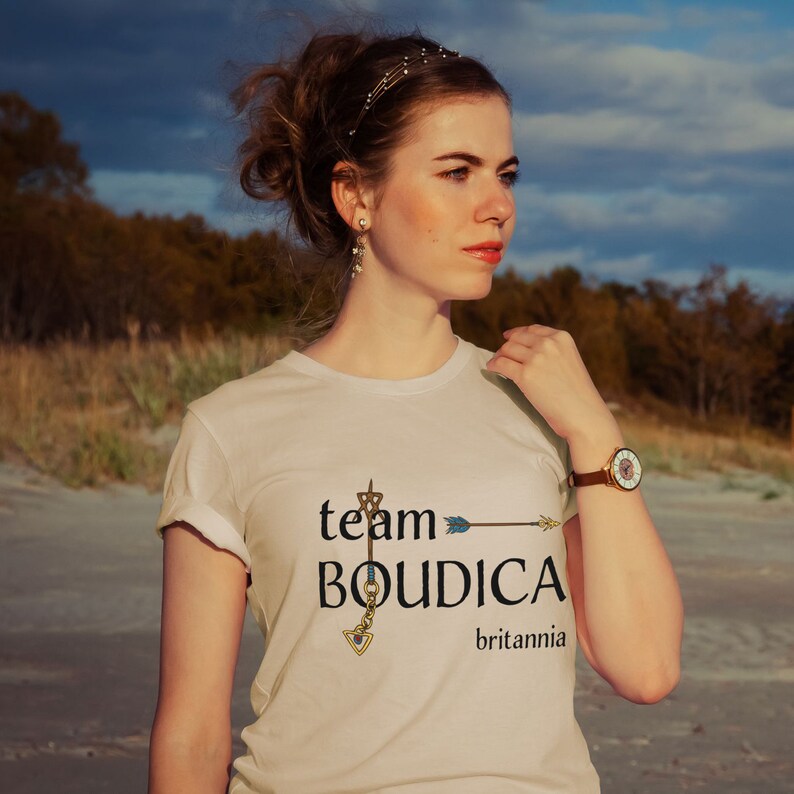 Pu&ograve; includere: Maglietta bianca con un design grafico che dice "team BOUDICA britannia" con una freccia e una stella.