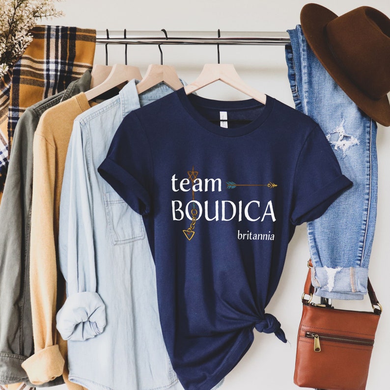 Pu&ograve; includere: Una maglietta blu navy con il testo "team BOUDICA britannia" e una grafica di freccia dorata.