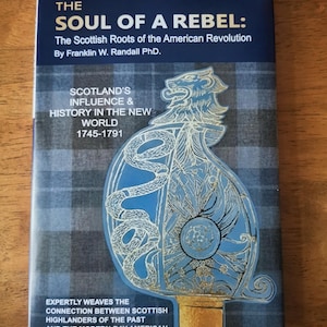 Puede incluir: Un libro titulado "The Soul of a Rebel" sobre las raíces escocesas de la Revolución Americana. La portada presenta una ilustración azul y dorada de una espada y un fondo con patrón de tartán. El libro explora la influencia de Escocia de 1745-1791.