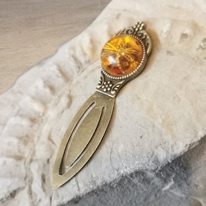 May include: A bronze bookmark with a round, amber-coloured glass cabochon featuring a dragonfly design.