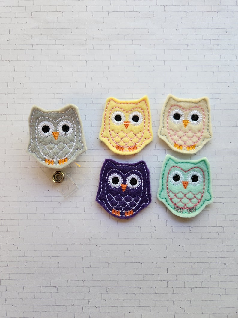 Puede incluir: Cinco portagajes de fieltro en forma de b&uacute;ho en diferentes colores: gris, amarillo, rosa, morado y verde. Cada b&uacute;ho tiene ojos bordados, un pico y un patr&oacute;n en su cuerpo.