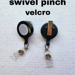 May include: Two black retractable badge reels with swivel clips and clear plastic badge holders. One reel has a velcro attachment and the other has a pinch clip.
