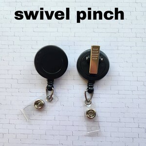 May include: Two black retractable badge reels with swivel clips and clear badge holders. The reels have a black plastic body and a silver metal clip. The badge holders are clear plastic and have a silver metal button.