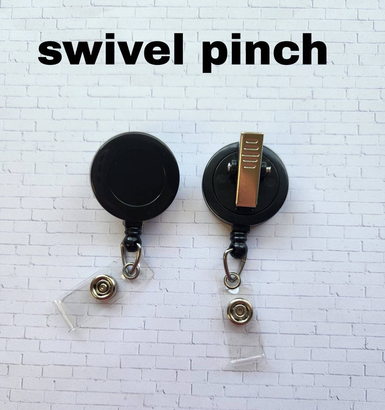 May include: Two black retractable badge reels with swivel clips and clear badge holders. The reels have a black plastic body and a silver metal clip. The badge holders are clear plastic and have a silver metal button.