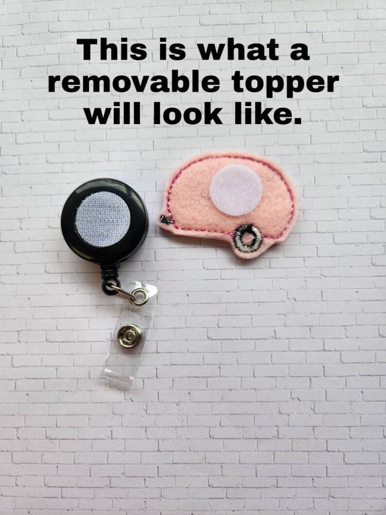 May include: A close-up of a pink felt camper van with a white circle in the middle. The camper van is attached to a black retractable badge reel with a clear plastic strap. The text "This is what a removable topper will look like." is visible at the top of the image.