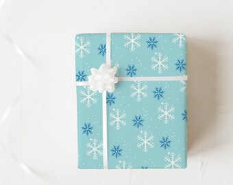 May include: A wrapped gift box with a light blue snowflake pattern. The gift is tied with a white ribbon and bow. The snowflakes are white and dark blue. The background is white.