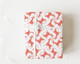 May include: A wrapped gift box featuring a white background with a repeating pattern of orange reindeer. The box is tied with a white ribbon and bow, creating a festive and decorative presentation.