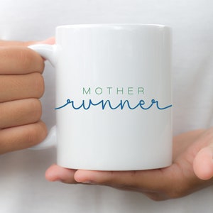 May include: White ceramic mug with a blue and green design that says "MOTHER runner" in a cursive font.