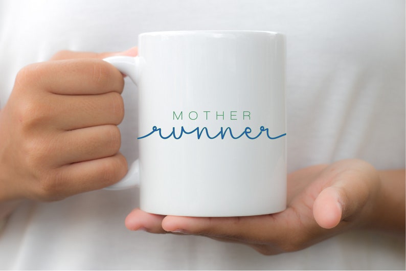 May include: White ceramic mug with a blue and green design that says "MOTHER runner" in a cursive font.