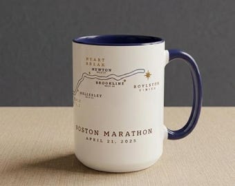 May include: White ceramic mug with a navy blue handle and interior rim. The mug features a map of the Boston Marathon route, with key locations labeled. Text on the mug reads "Boston Marathon April 21, 2025."