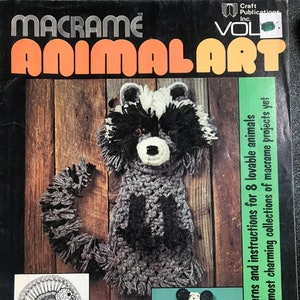 May include: A book cover with the title "Macrame Animal Art" and a picture of a raccoon, a turkey, a snail, and a panda bear. The book is volume 1 of a series by Craft Publications Inc.