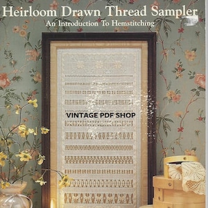May include: A framed sampler featuring a range of drawn thread embroidery stitches. The sampler is titled "Heirloom Drawn Thread Sampler" and "An Introduction to Hemstitching". The sampler is in a wooden frame and is displayed against a floral wallpaper.