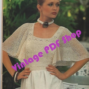 May include: A woman wearing a white crochet top with a shell necklace and a white skirt. The top has a wide, open neckline and a loose, flowing fit. The skirt is simple and elegant. The woman is standing in a garden setting.