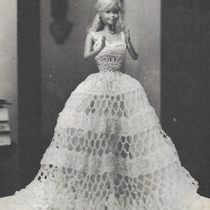 May include: A white crocheted doll dress with a lacy design. The dress has a fitted bodice and a full skirt.