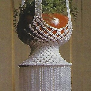 May include: White crocheted hanging plant holder with a green plant inside. The holder has a fringe at the bottom.