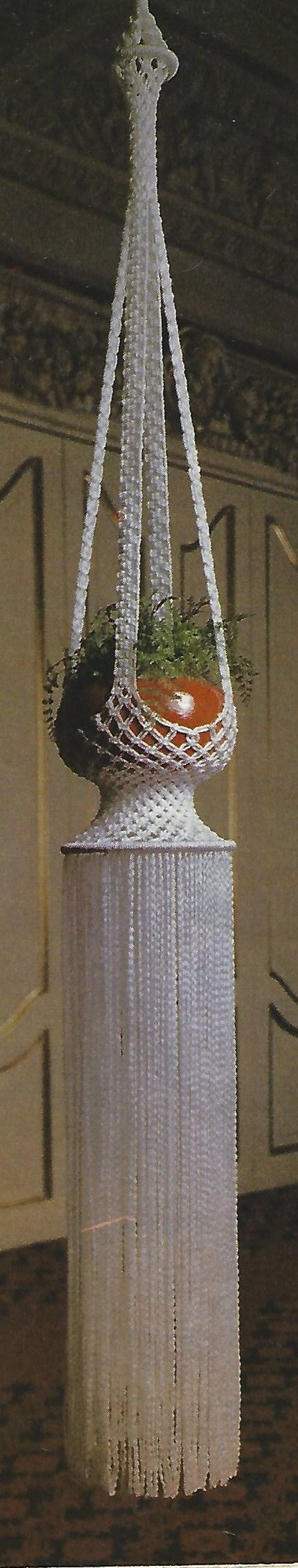 May include: White crocheted hanging plant holder with a green plant inside. The holder has a fringe at the bottom.