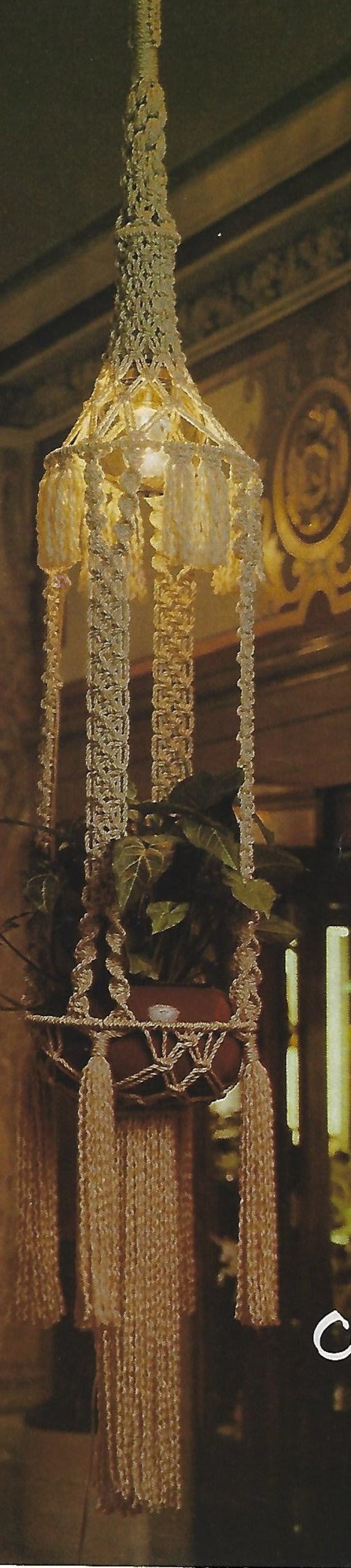 May include: A macrame plant hanger with a white and cream color scheme. The hanger is made of knotted cords and has a round pot at the bottom. The hanger is hanging from the ceiling and there are green plants growing in the pot.