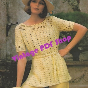 May include: A crochet top with a wide, round neckline and short sleeves. The top is made of a light yellow yarn and has a crocheted belt. The model is wearing the top with a straw hat and yellow pants.