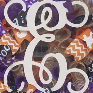 May include: White wooden letter "E" with a cursive font, surrounded by orange, purple, and brown burlap ribbon with a black and white polka dot pattern and a black and white chevron pattern. The ribbon has a ghost and "BOO" printed on it.