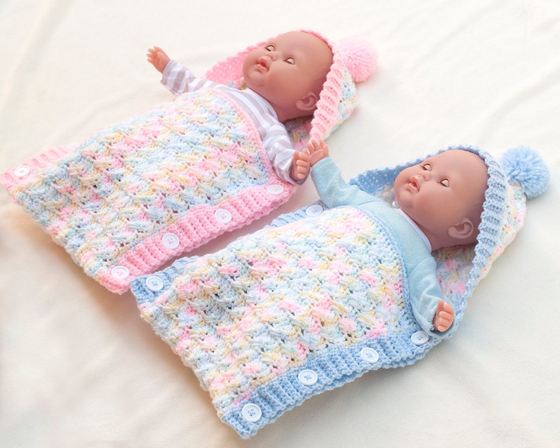 May include: Two crocheted baby sleeping bags with hoods, one pink and one blue, with white buttons. The sleeping bags are made with a textured stitch and have a colorful yarn pattern.