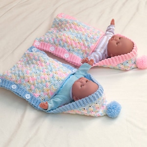 May include: Two crocheted baby sleeping bags with hoods and pom-poms. One is blue with white buttons and the other is pink with white buttons.