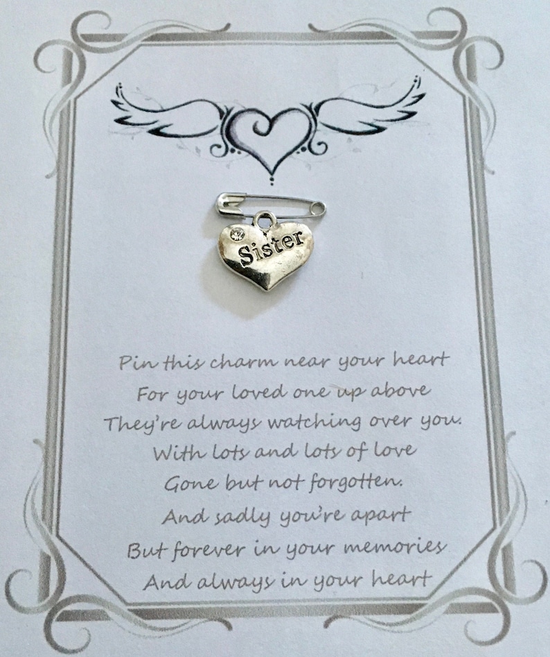 May include: A silver heart-shaped charm with the word "Sister" on it, attached to a safety pin. The charm is on a card with a heart and wing design, and a poem about remembrance.