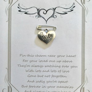 May include: A silver heart-shaped charm with the word "Wife" and a small crystal, attached to a safety pin. The charm is on a white card with a decorative border, a heart and wing design, and sentimental text.