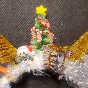 May include: A white Christmas wreath with a miniature snowman, a small Christmas tree with candy canes, a silver gift box with gold ribbon, and a gold glitter snowflake.