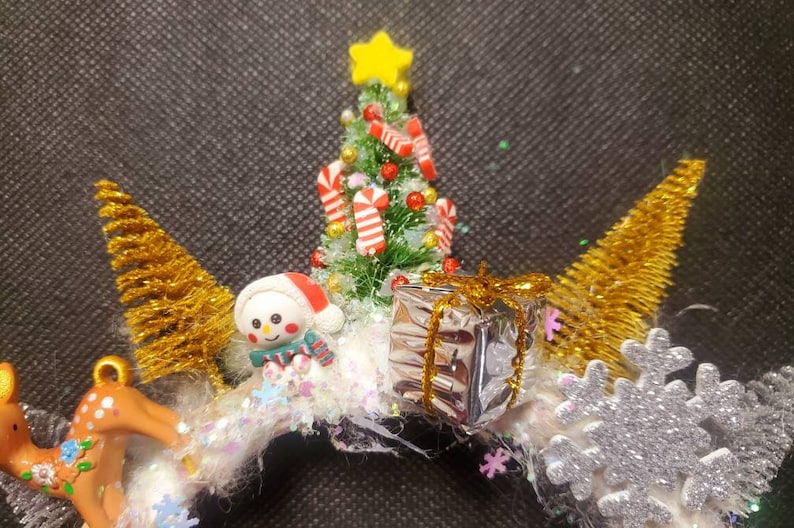 May include: A white Christmas wreath with a miniature snowman, a small Christmas tree with candy canes, a silver gift box with gold ribbon, and a gold glitter snowflake.