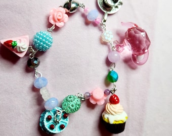 May include: A charm bracelet with a teacup, teapot, cupcake, cake, and flower charms. The bracelet is made with silver chain and colorful beads.