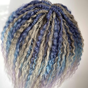 May include: A bundle of synthetic dreadlocks in shades of blue, gray, and lavender. The dreadlocks have a curly texture and are arranged in a circular shape. The colors blend together, creating a gradient effect.