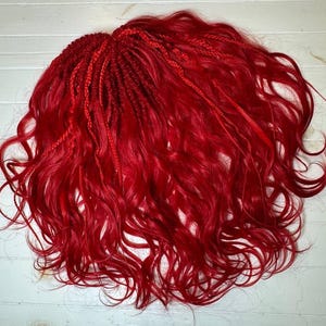 May include: Bright red, wavy hair extensions with a braided top section. The extensions are arranged in a loose, flowing style, with a mix of braids and loose waves. The hair is a vibrant, solid red color.