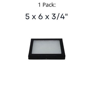 Op de afbeelding: Zwarte vierkante displaykoffer met een wit schuim interieur. De koffer meet 12,7 cm bij 15,2 cm bij 1,9 cm.